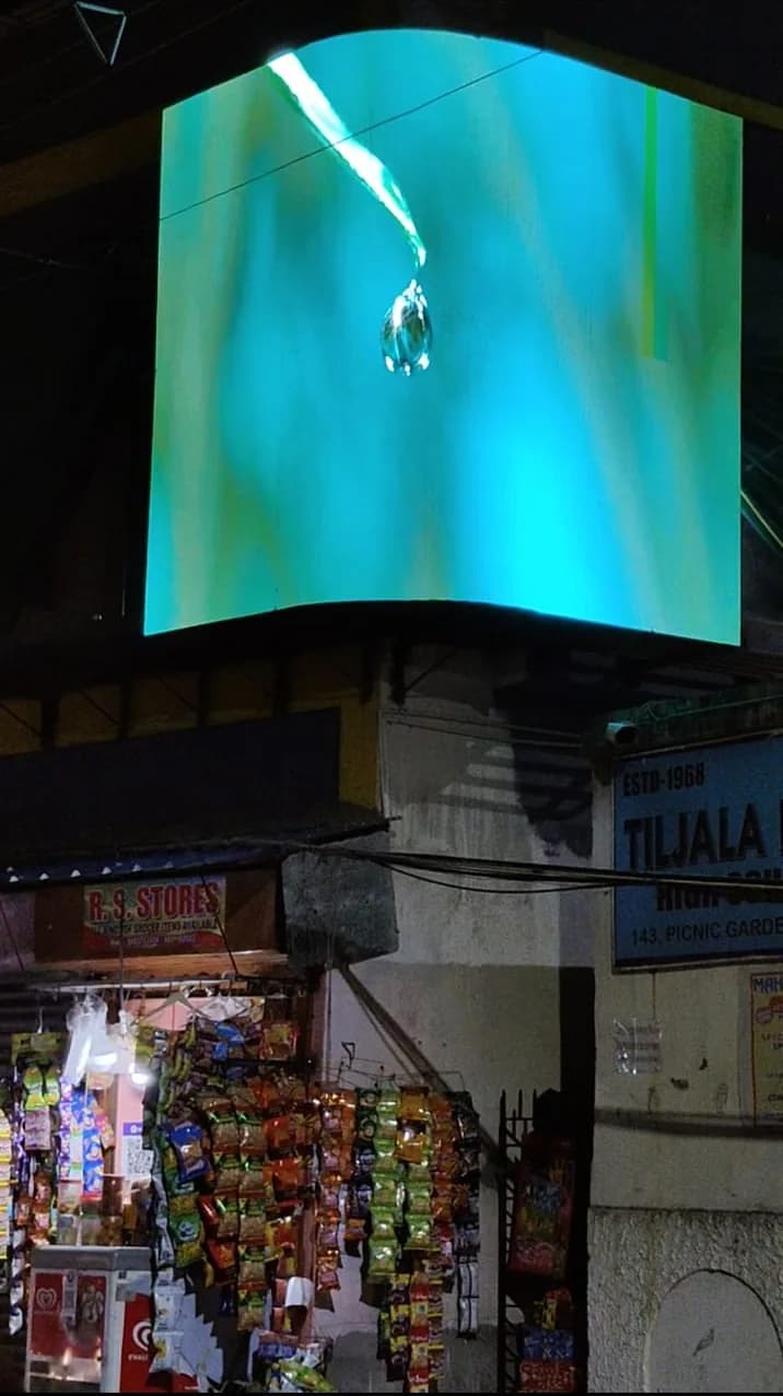 Curved outdoor LED screen on a corner building at night showing a water drop on a leaf