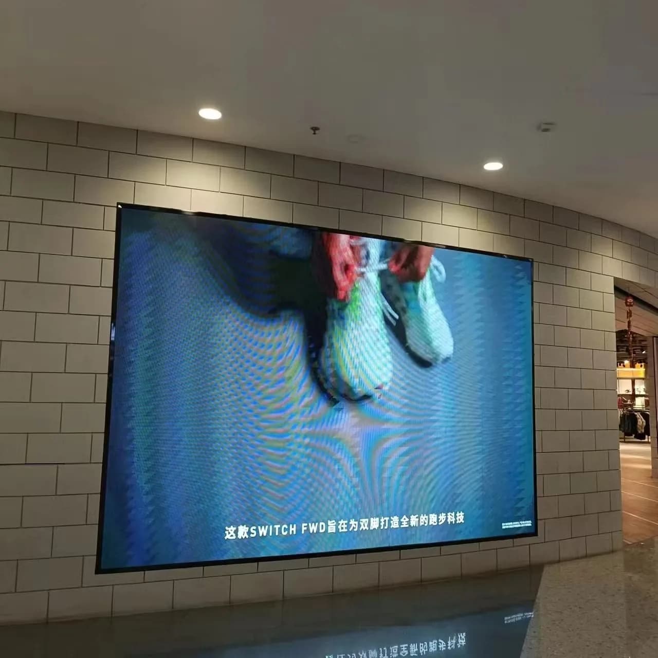 Large LED screen on a mall wall showing a pair of sneakers