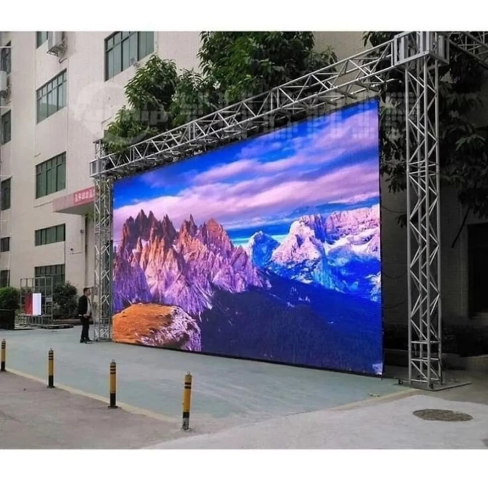 Large outdoor LED screen on a truss in front of a building, showing mountains
