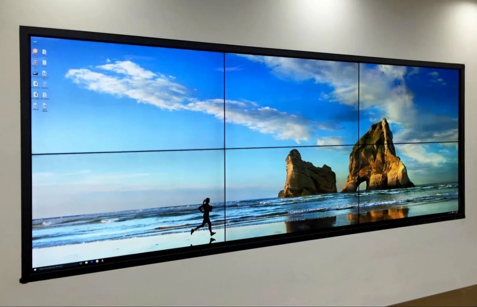 Wall-mounted video wall made of panels showing a beach and rock stacks