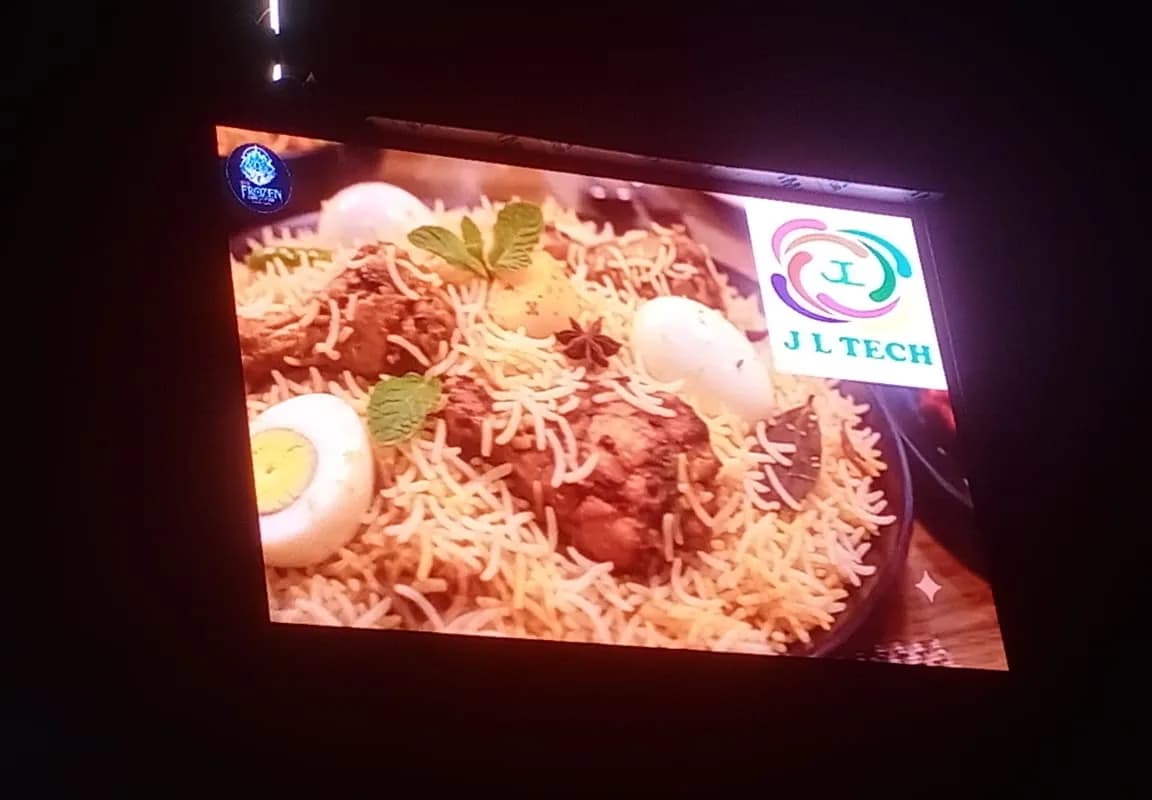 Outdoor LED screen at night showing a food advert with the J L Tech logo in the corner