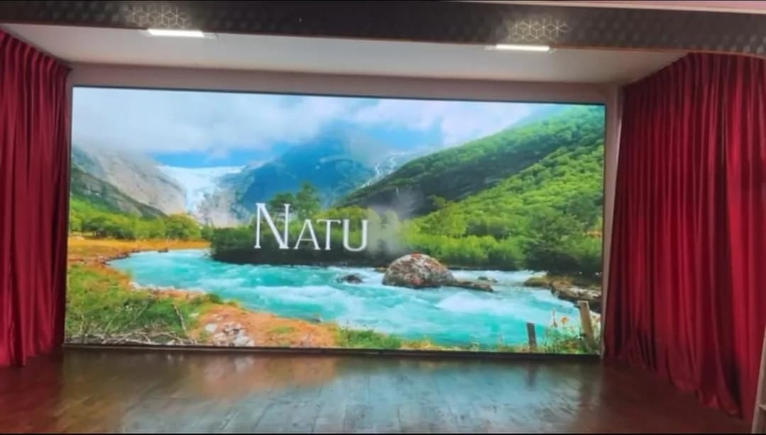 Indoor LED wall on a stage between red curtains showing a mountain river landscape