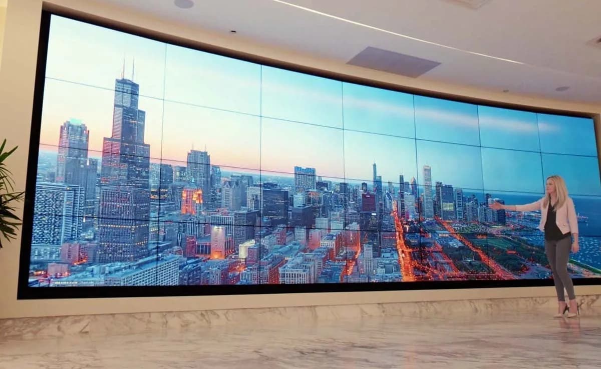 Curved video wall in a lobby showing a city skyline, with a presenter beside it